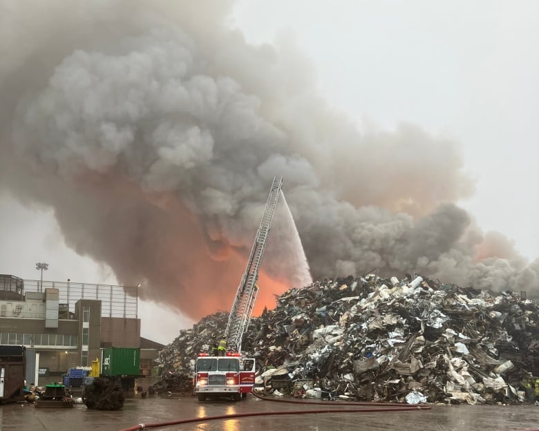 Smoke billowing out of a large pile of metal, fire truck pouring liquid onto it