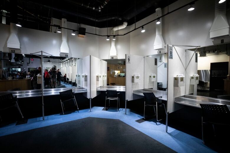 A wall of cubicles with chairs and safe deposit boxes for used needles.