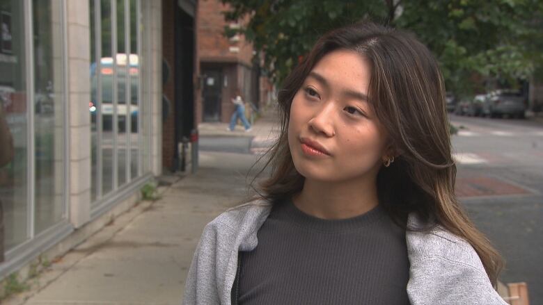 A close-up screengrab of a woman standing on a sidewalk. 