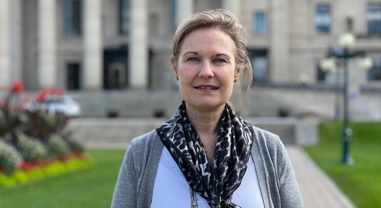 A woman wearing a scarf and cardigan stands in front of a legislative building.