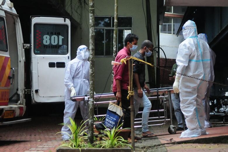 People walk from an ambulance into a hospital by people wearing full protective equipment