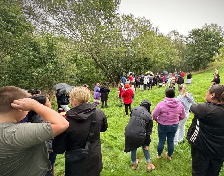 A group of people gather on the grass near the woods next to a creek.