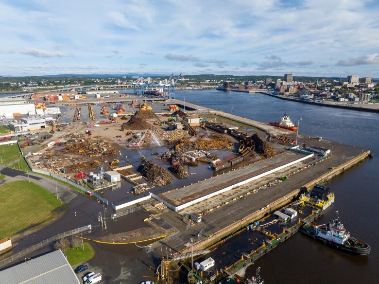 Areal shot of a scrap yard overlooking the harbour, showing fire trucks pouring liquid over charred metal