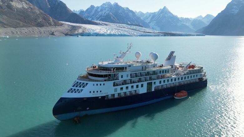 A large cruise ship sails through Arctic landscape on blue waters.