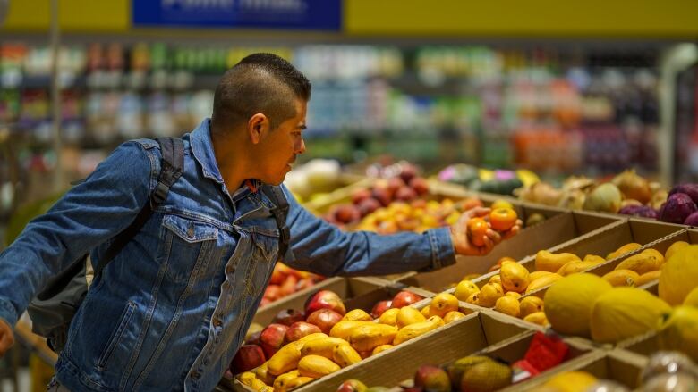 A man picks up some fruit in a grocery store's produce section.