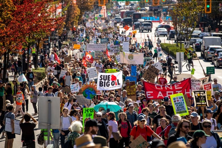 A large crowd of people march with various colourful signs held above their heads. 