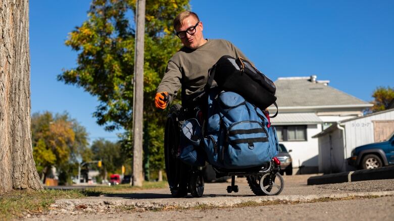 A man in a wheelchair points at a broken piece of sidewalk.