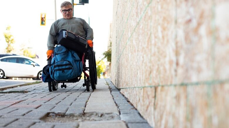 A man in a wheelchair looks at a missing chunk of sidewalk heading downhill.