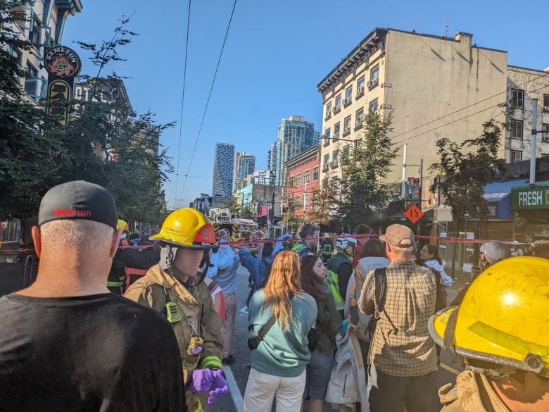 Firefighters and onlookers mill around on a street.