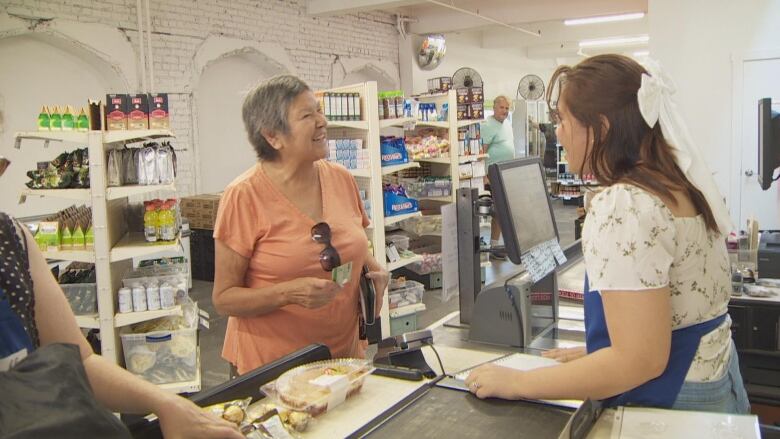 An older woman smiles at a cashier at a grocery check-out counter. 