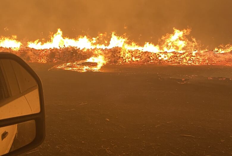 Looking out a vehicle window at piles of logs on fire in the dark.