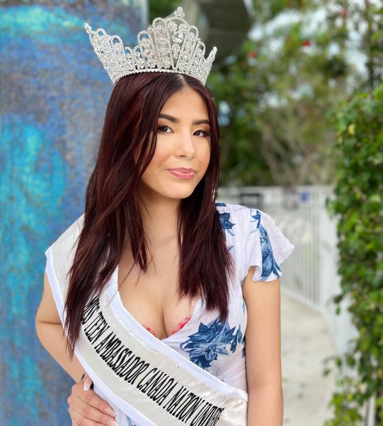 A Cree beauty queen, wearing a shash and a crown looks straight into the camera.