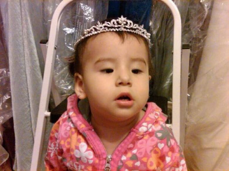 A Cree toddler in a stroller wears a crown.