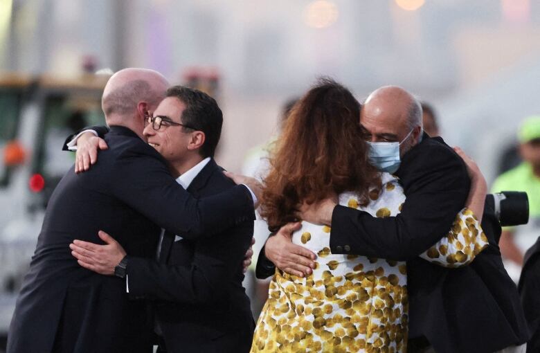 On the left, two men hug. Next to them, a man and a woman hug. 