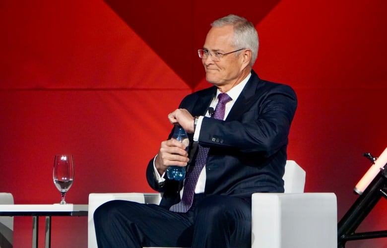 An oilpatch executive opens a bottle of water while on stage at a conference.