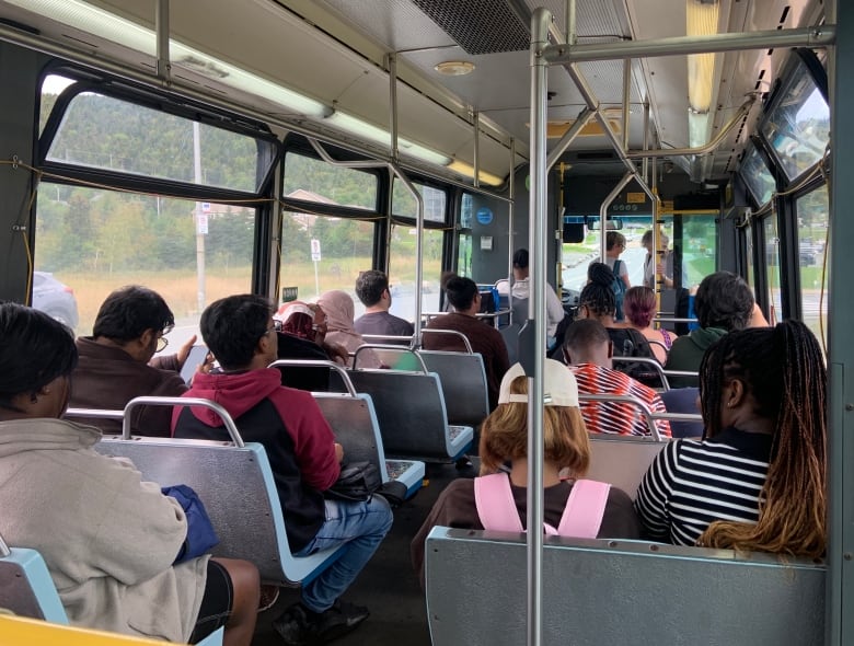 The inside of a bus. Most, but not all seats are full.