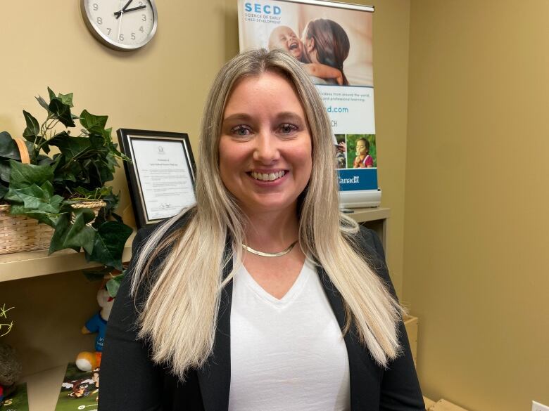 A smiling woman with blonde hair down to her chest stands in an office space.