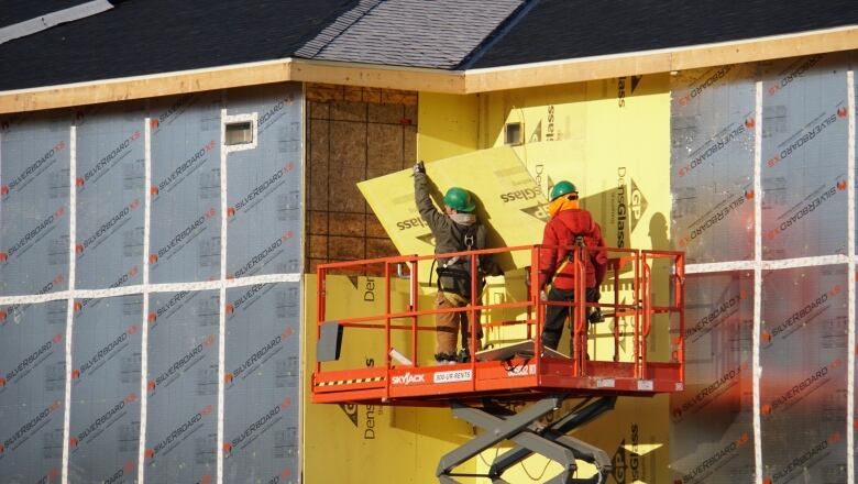 Some workers stand on a scissor lift, putting panels into place on an unfinished building