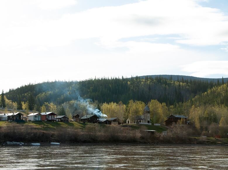 A small group of buildings are seen on the bank across a river.