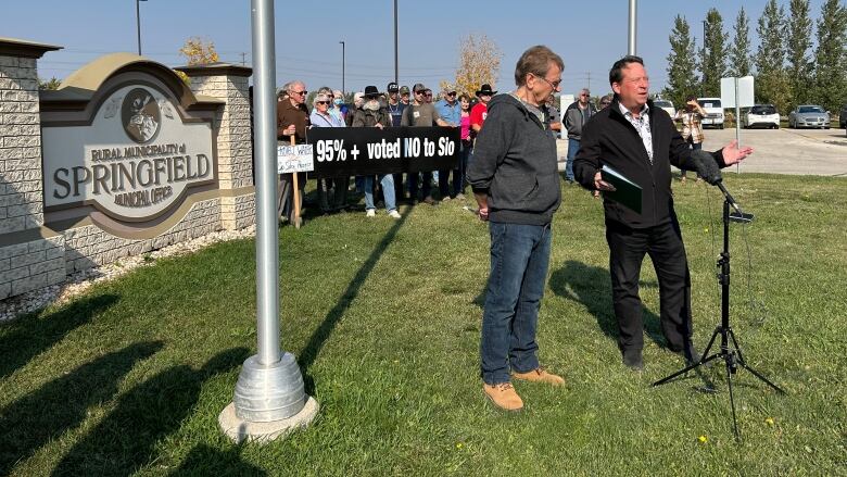 A group of people stand behind to politicians outside a community council building.