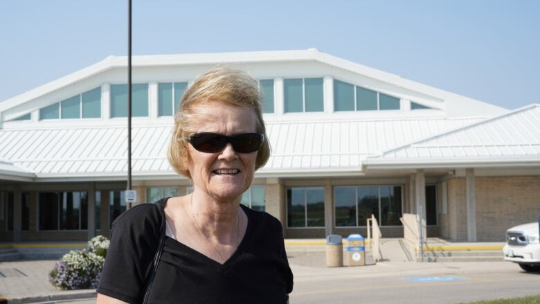 A woman with short blond hair wearing sunglasses stands in front of a council building.