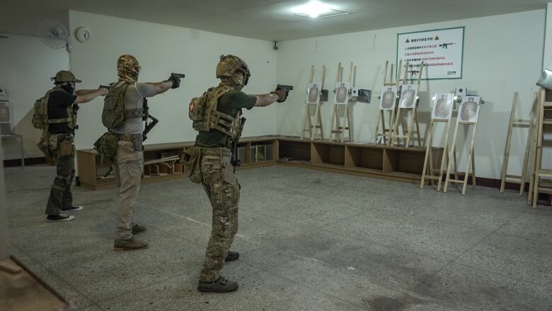 Three people in camouflage take aim with pistols at indoor targets.