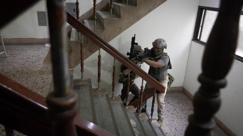 Two men with guns are pictured on a set of stairs.