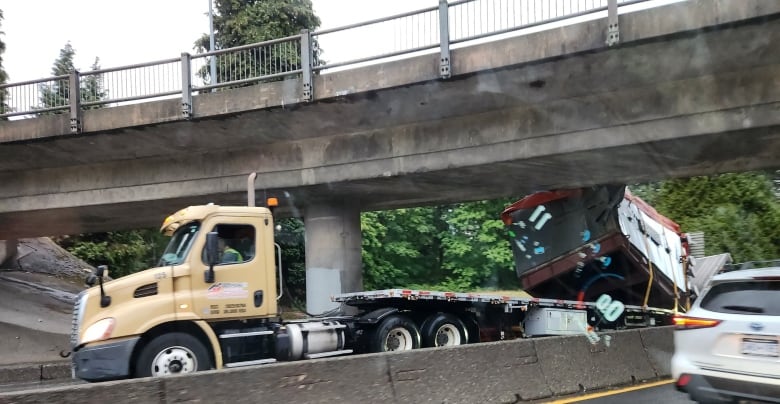 A truck which has just collided with an overpass is seen on a road, with a red payload behind it.