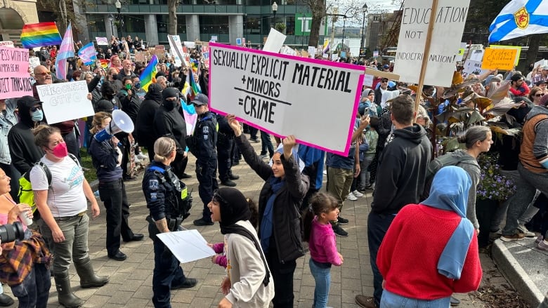 Two groups of people holding placards and flags are shown, with police officers standing between them.