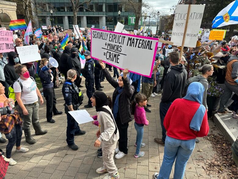 Two groups of people holding placards and flags are shown, with police officers standing between them.