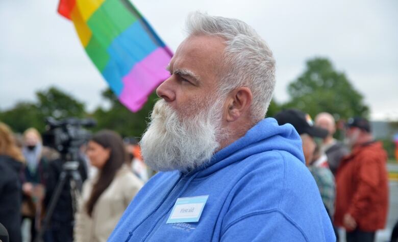 A man with a white beard and blue sweater stands among a group of protestors. 