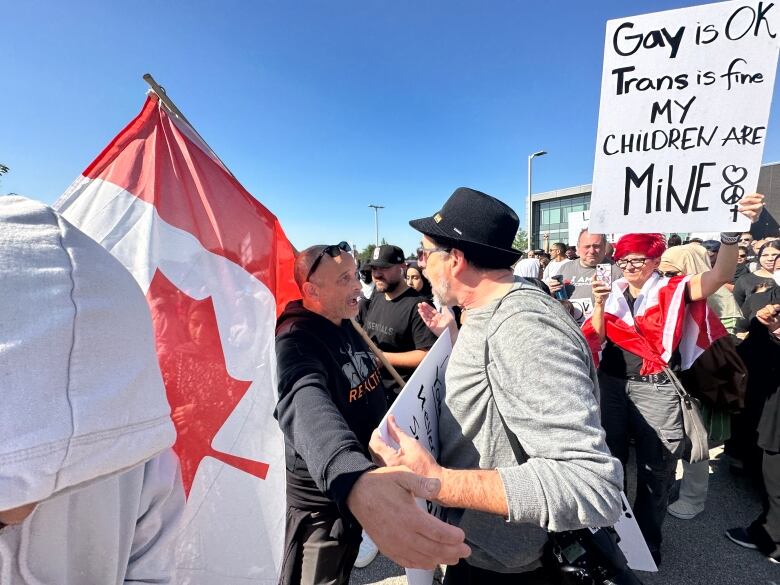 One person holding a Canadian flag speaks to a person holding a sign.