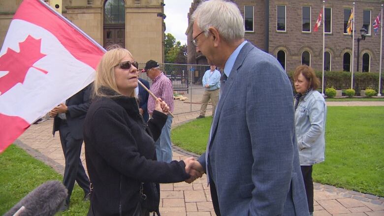 Man shaking hands with woman holding Canada flag over shoulder