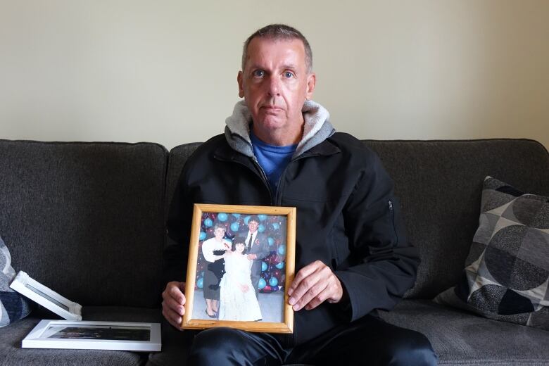 A man holds a framed photo sitting on a couch