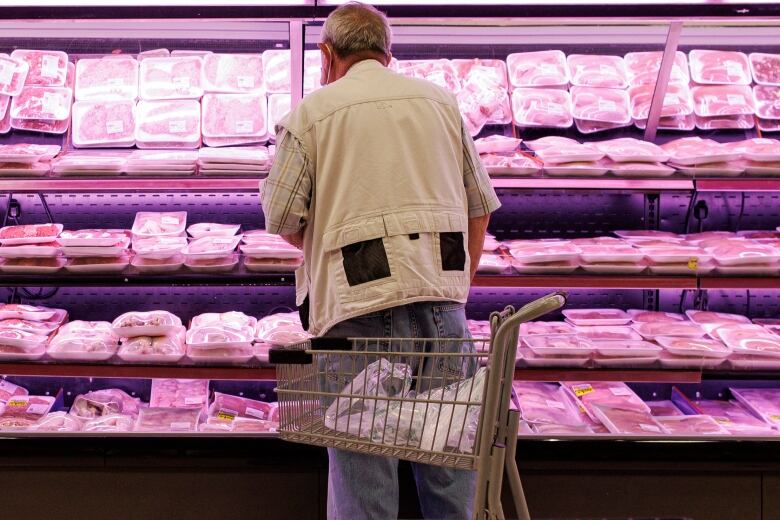 A senior looks over prices of meat in a supermarket. 