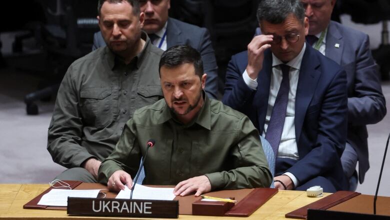 Zelensky, dressed in trademark olive shirt, speaks from desk