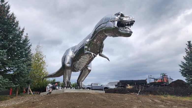 A giant metal T-rex stands on a concrete platform with trees beside him. 