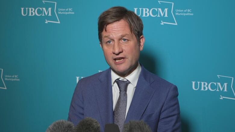 A white man speaks in front of a blue background.