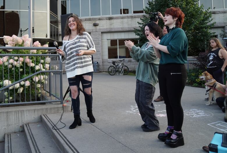 Three people stand outside a building, cheering.