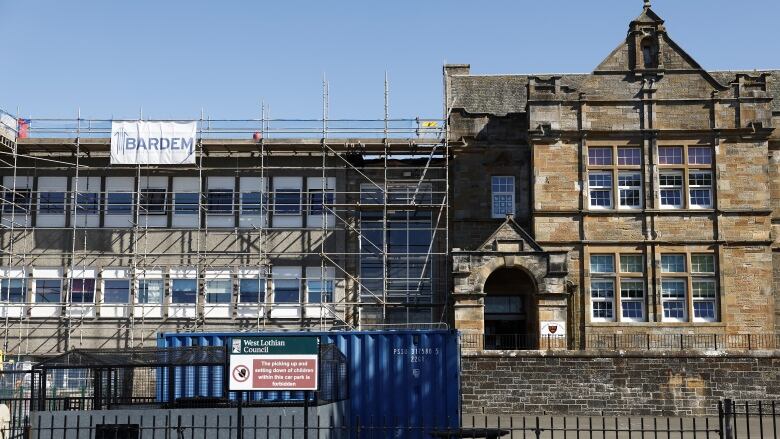 The concrete exterior of a school building is covered in scaffolding. 