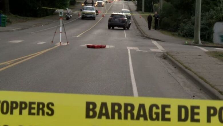 Yellow police tape on a street with officers in the background. 