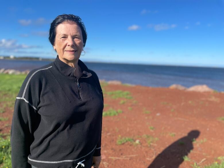 Myrna Gough wears a black jacket, and looks at the camera.  Her property's water view is visible over her shoulder. 