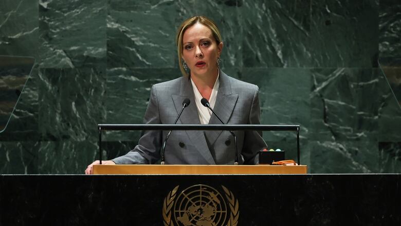 A woman in a suit speaks at a podium.