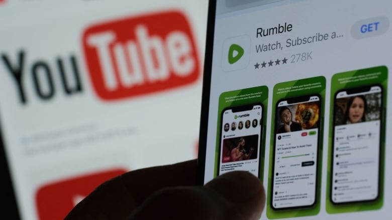 A phone is displayed in closeup displaying the Rumble video site app in an app store.