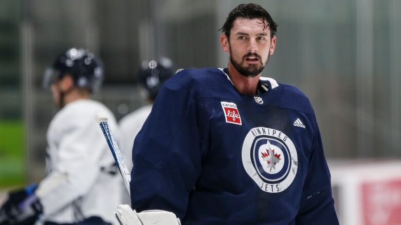 Bearded goaltender stands with his mask off during a break in practice.