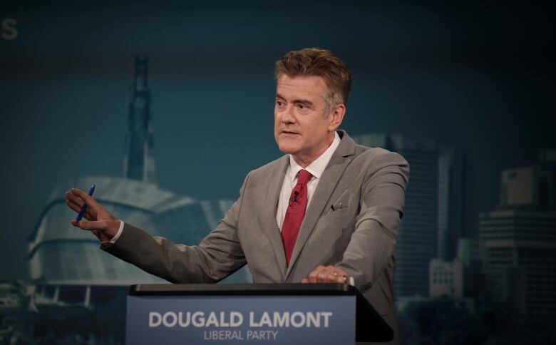 A man in a suit speaks at a podium.