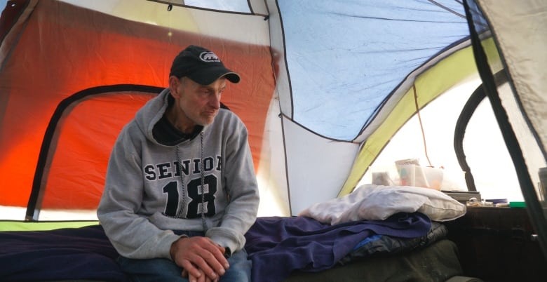 A man sits on an elevated bed in a tent.