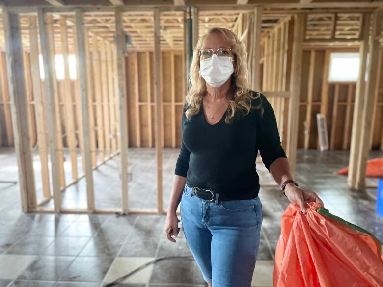 A woman wearing a black shirt and jeans stands in a building that has exposed wooden beams.