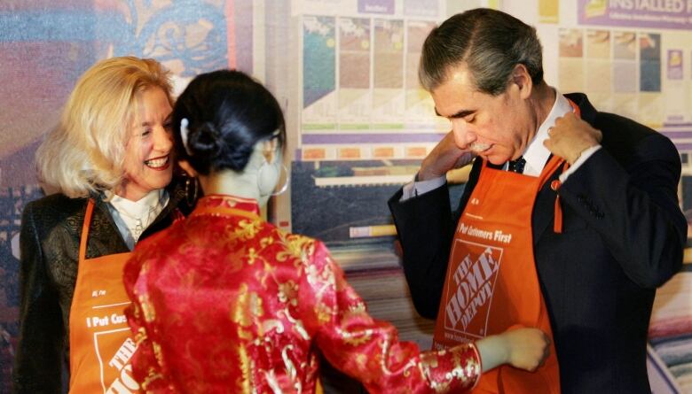 Two people wearing orange aprons stand next to a woman in a red dress.