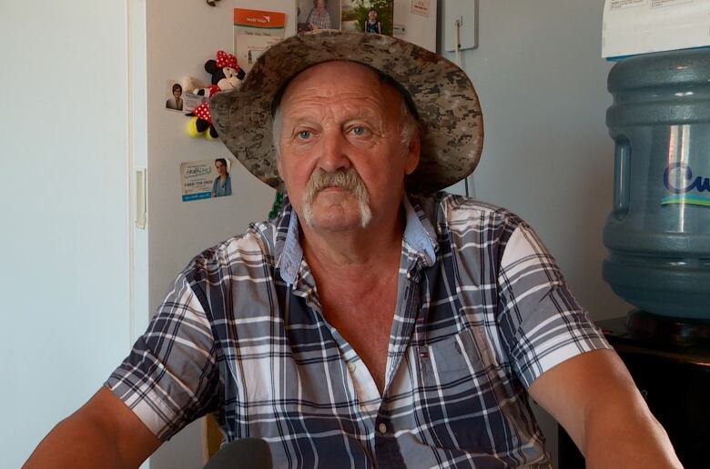 A man in his 60s wearing a straw hat and a button up shirt. He is sitting at his dinner table. 